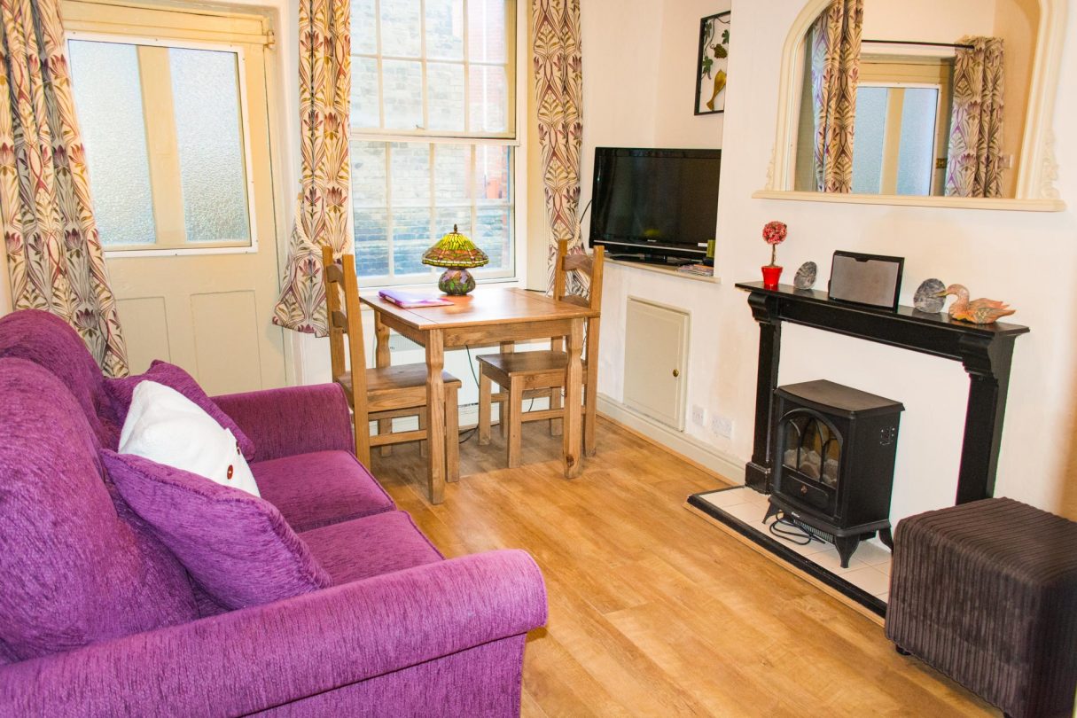 Living area of Fisherman's Cottage, featuring a purple sofa, and dining area.
