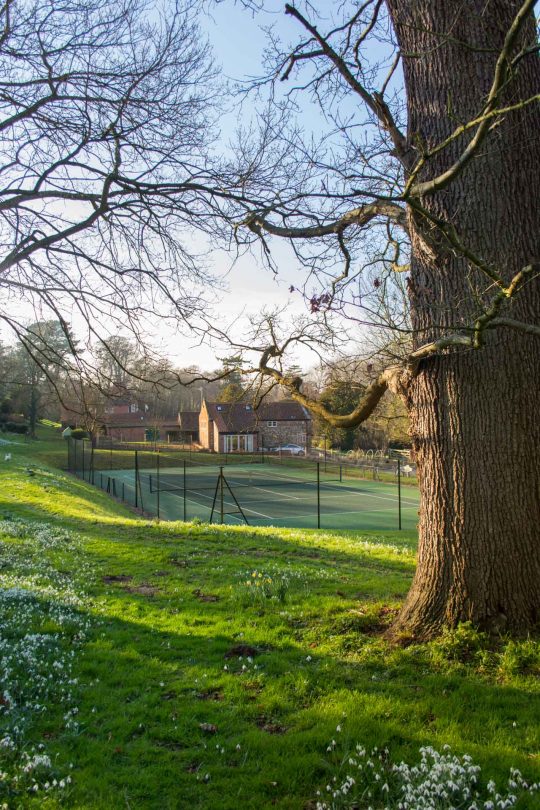 Long distance photo of the tennis court and Boathouse Barn from the woods.