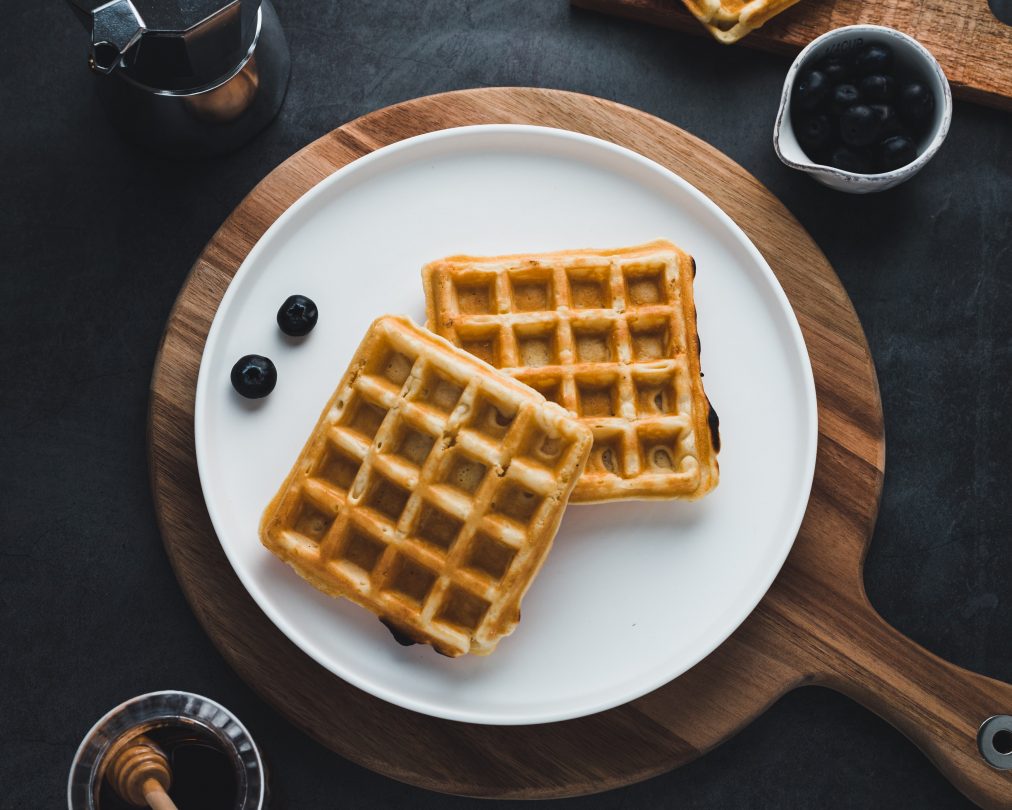 A plate of two waffles on a wood chopping board with berries and a side of syrup.