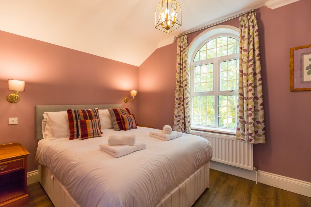 Redwings holiday apartments bedroom with white linen and pink walls.