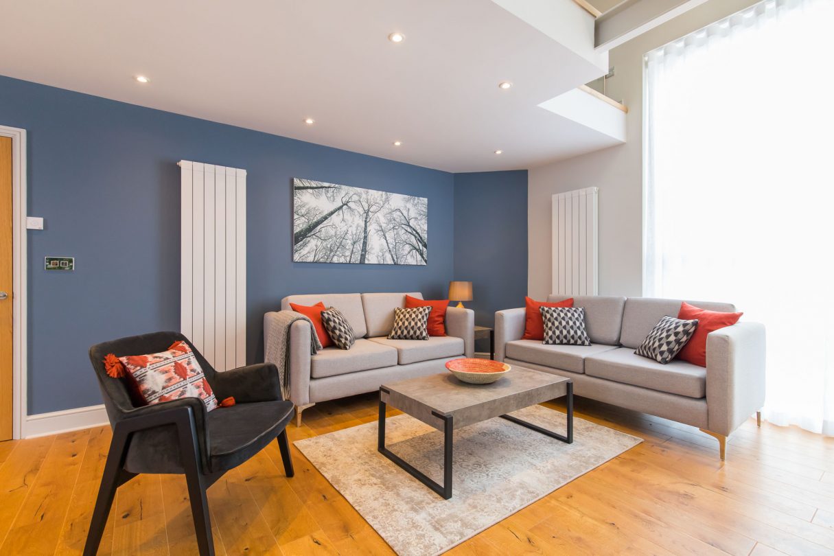 Holt holiday cottage living room with hardwood floors, grey sofas and red cushions.. 