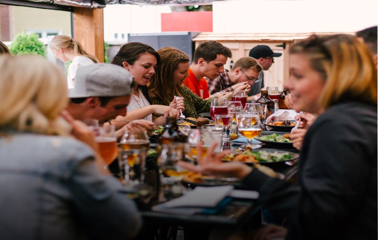Large group of people sharing a table eating, drinking and enjoying themselves.