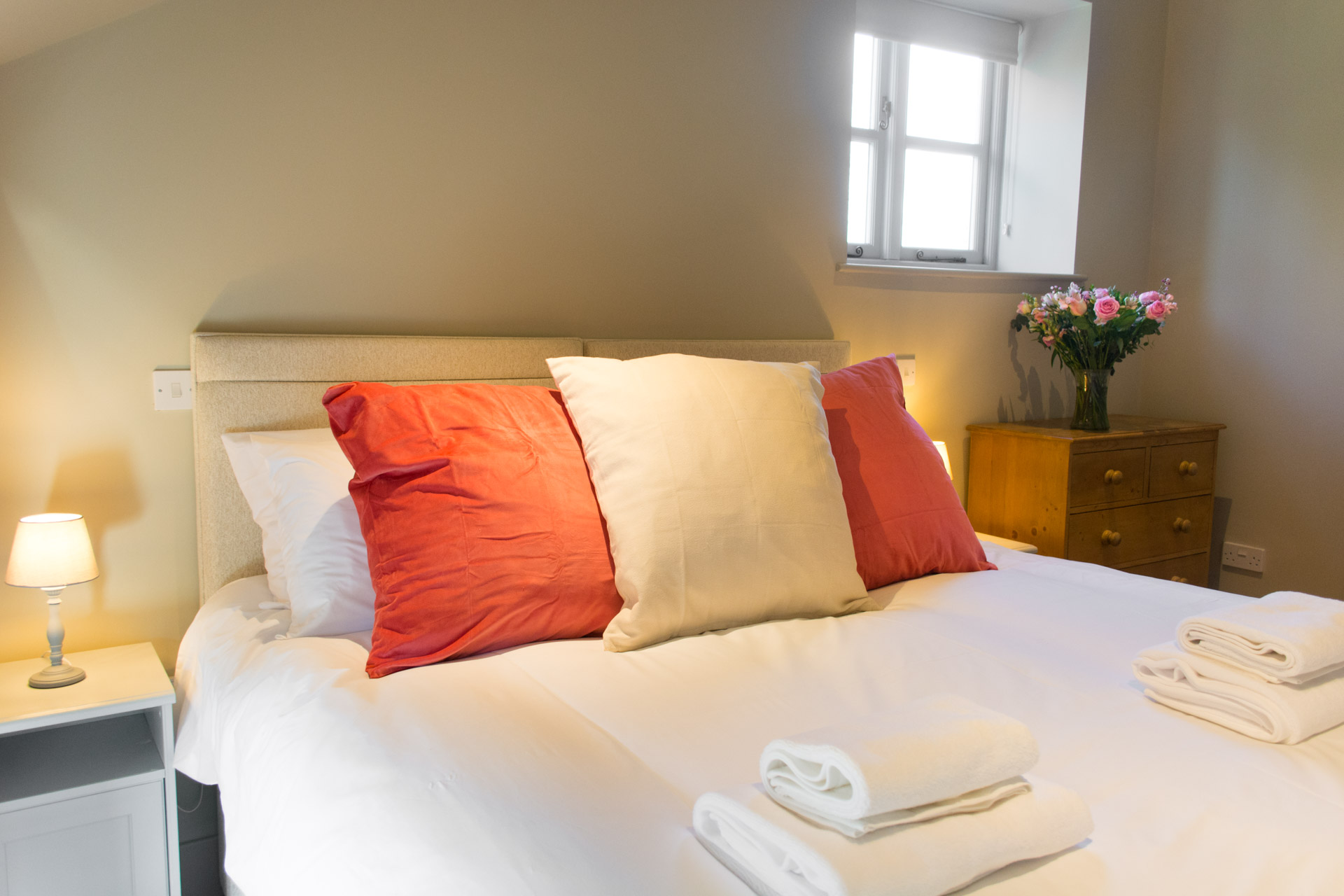 Close up of large red and white pillows with towels laid on the bed.