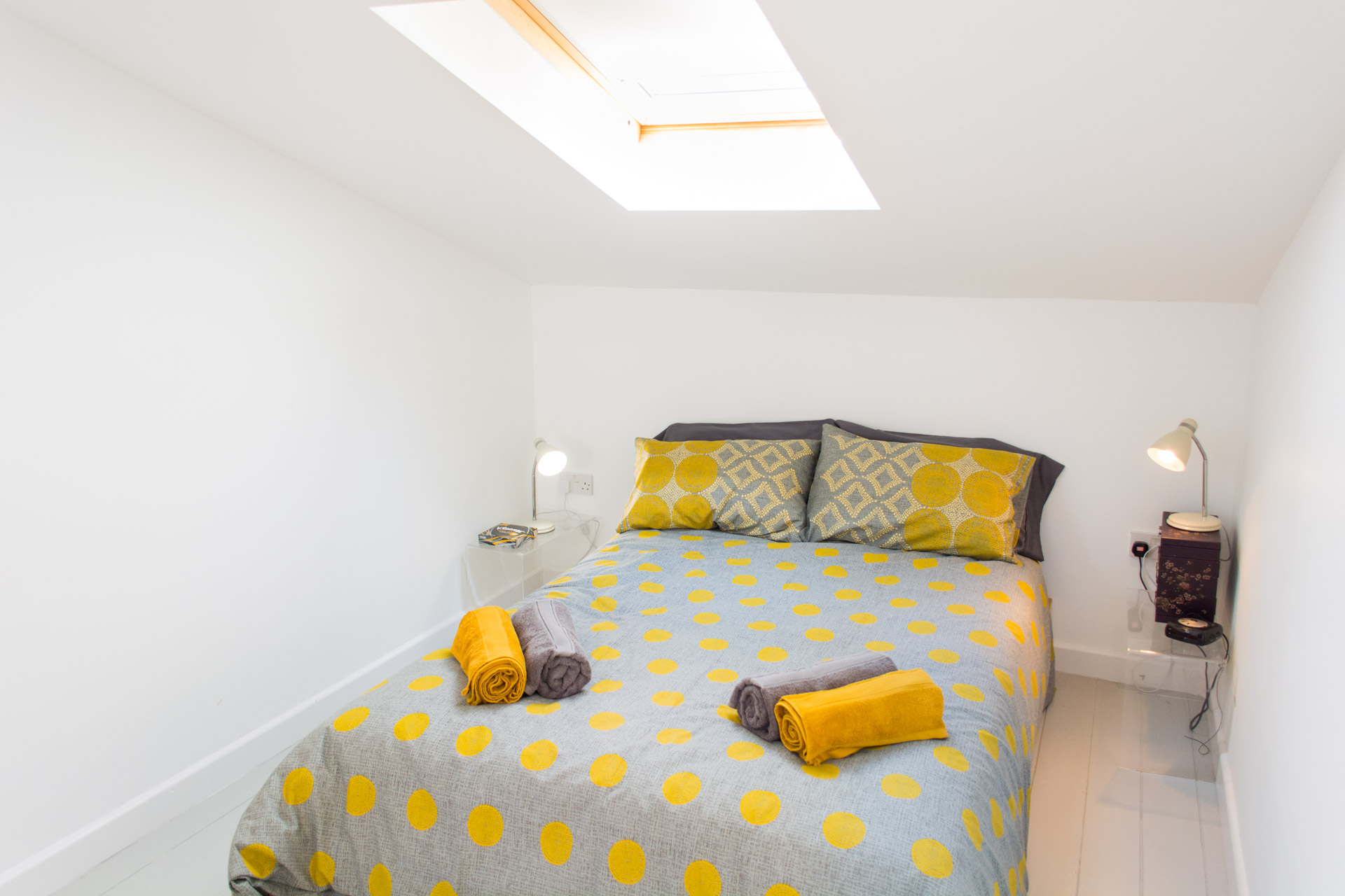 Second bedroom with ceiling window over the bed, decorated in an orange and grey duvet and pillow covers.