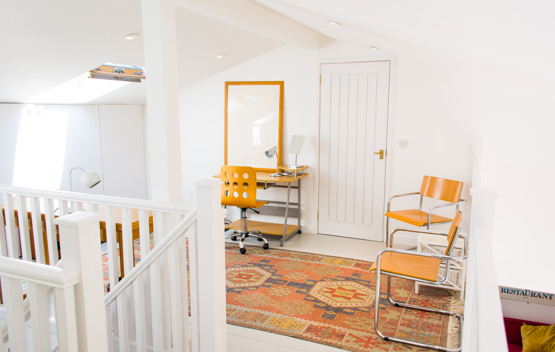 Upstairs hallway photo showing stair Bannister and chairs and table in the background.