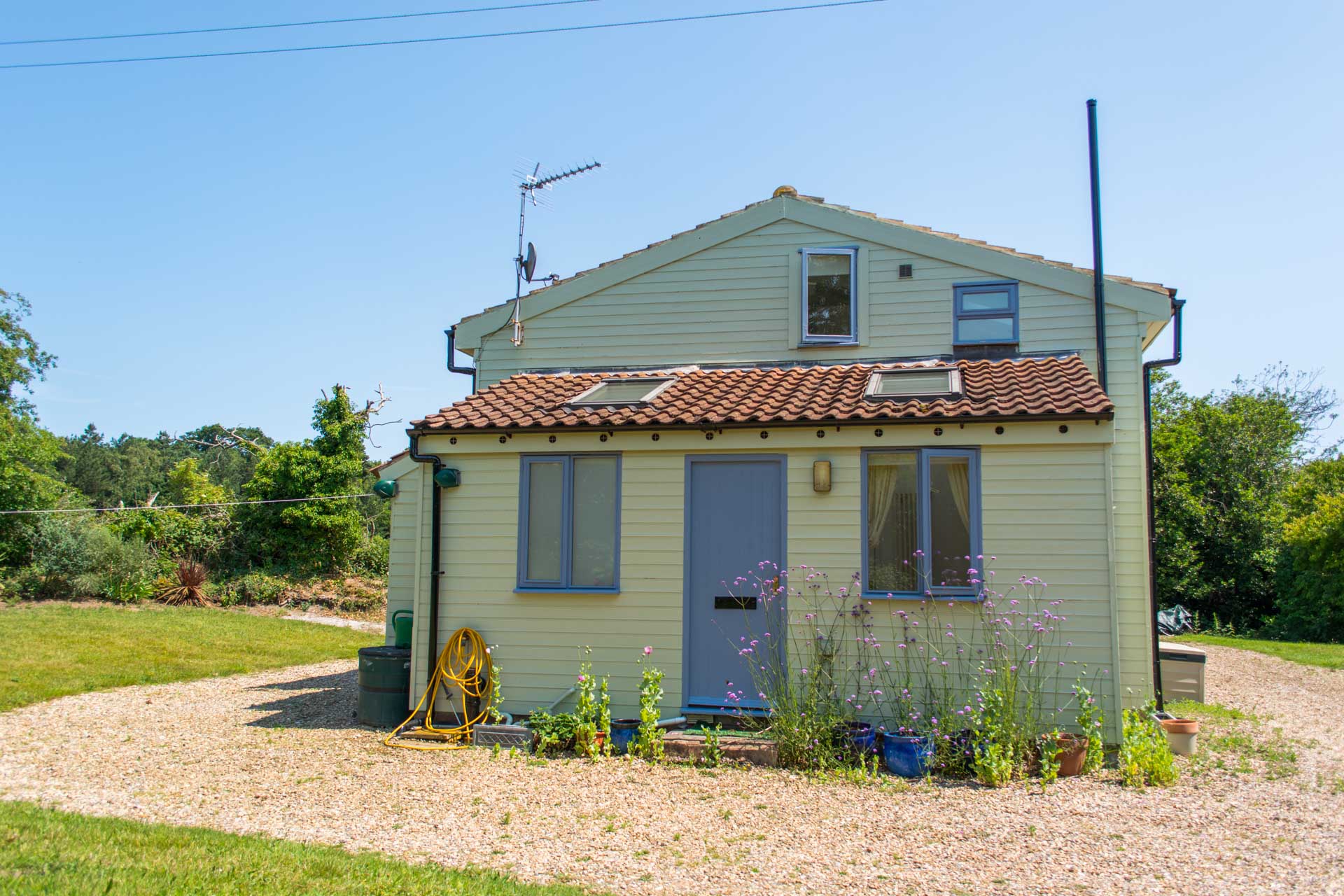 Outside photo of Holiday cottage showing the entrance doorway in front of gravel footpath and garden.